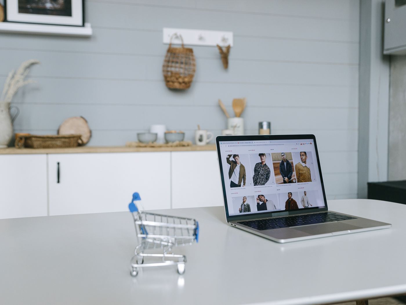 An online clothing store on a laptop beside a miniature shopping trolley