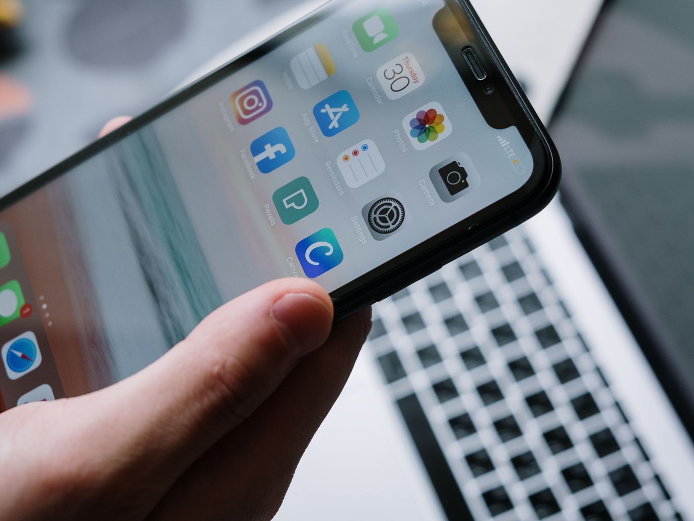 A phone showing its app grid, held above a laptop